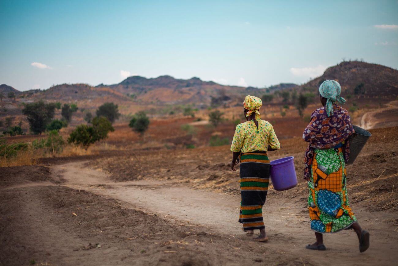 Women in brightly coloured clothes carry water buckets through the Malawian countryside.