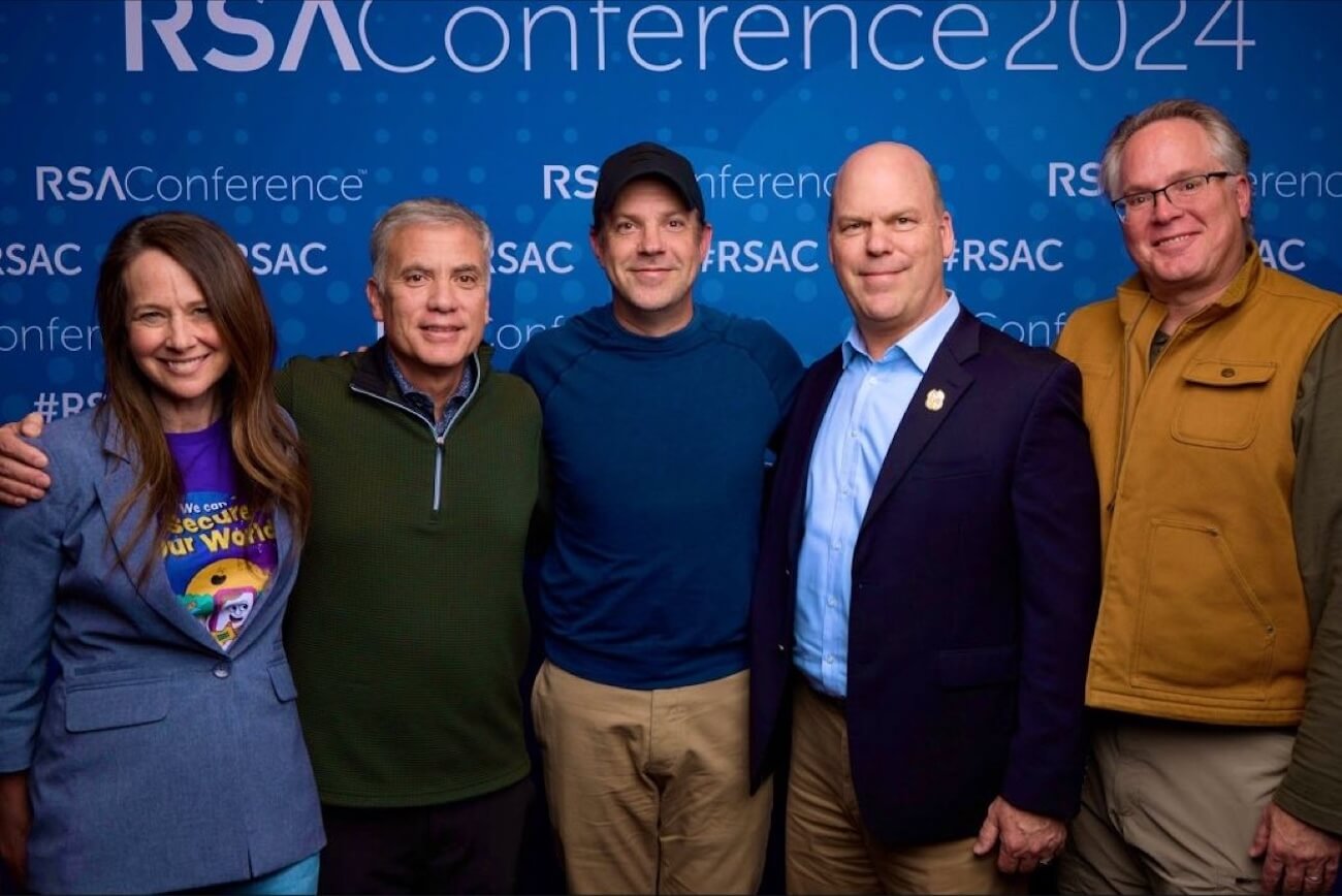 Actor Jason Sudeikis stands in front of an RSA Conference banner with CISA director Jen Easterly, among others.
